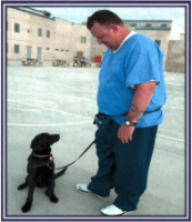 Incarcerated man stands with dog during training session.