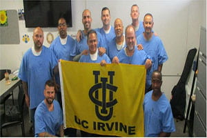 Group of incarcerated men hold gold and blue UC Irvine flag in front of them.